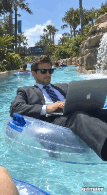 A drunk businessman in a suit on a laptop, floating down a lazy river drinking a beer